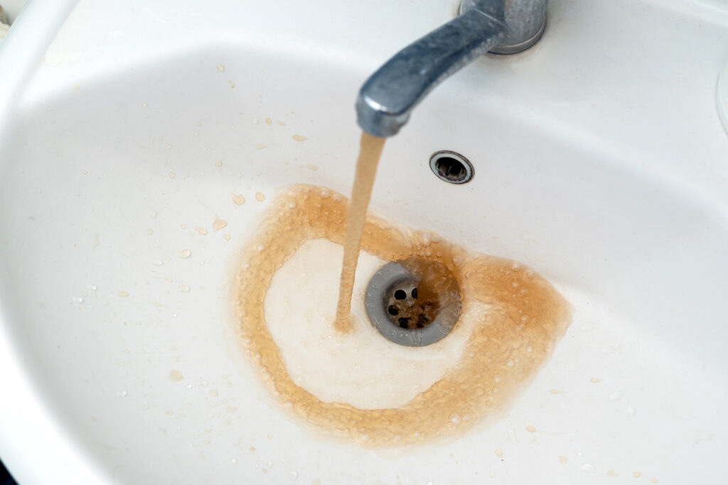 Bathroom faucet with brown hot water coming out of the tap