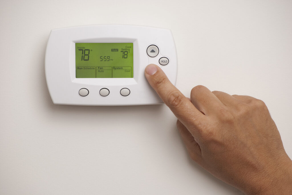 Man's hand turning on the AC thermostat for the first time after winter